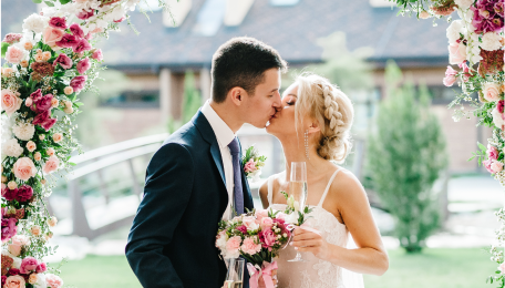 Bride and groom kissing under an arch lined with flowers